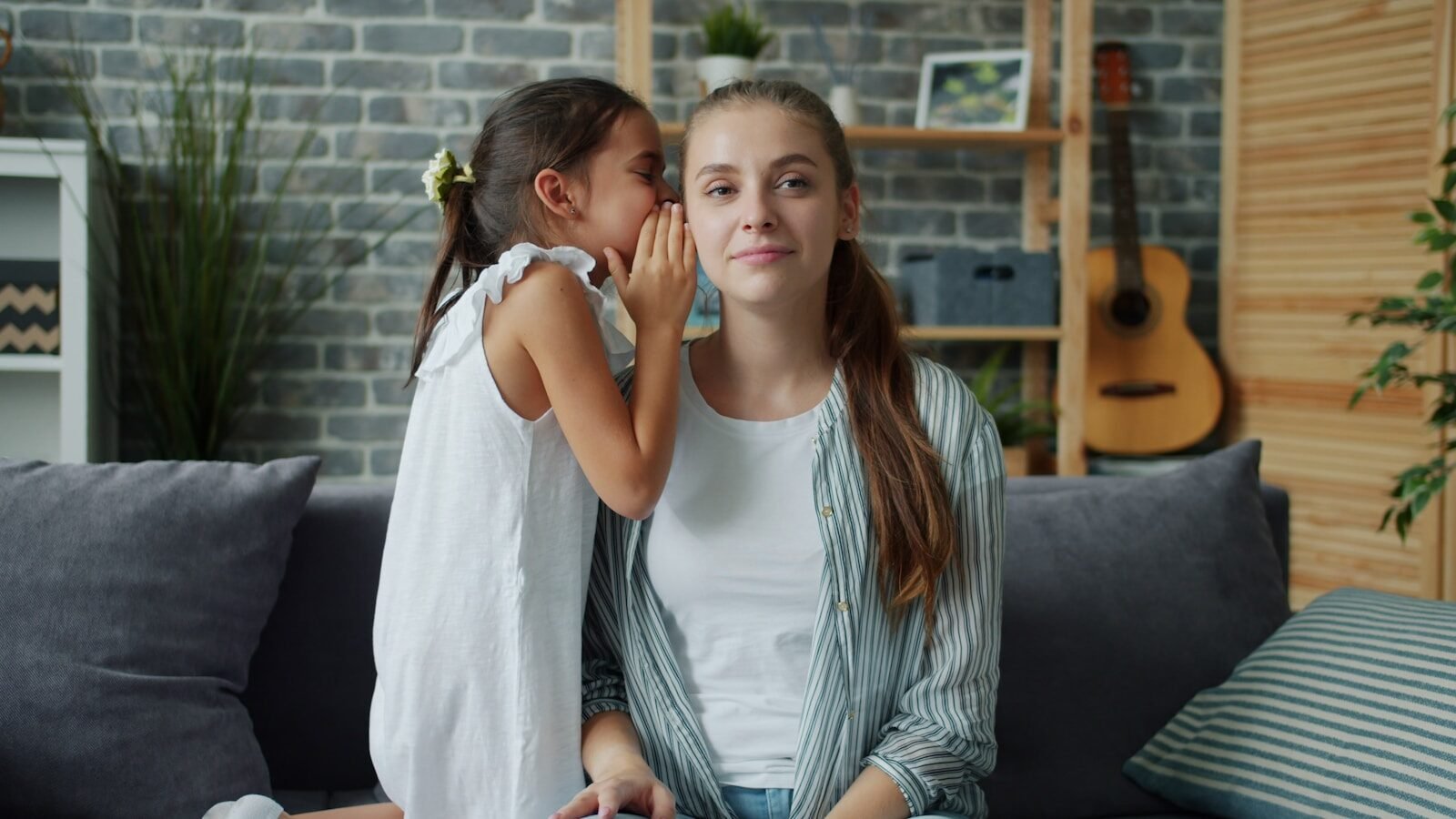 Girl whispers a secret into a woman's ear